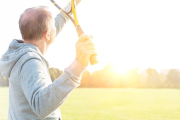 Senior man serving badminton in park on sunny day