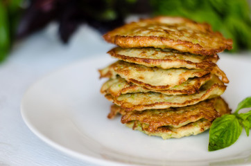 vegetarian zucchini pancakes, served with fresh herbs in the white plate and on the white wooden background