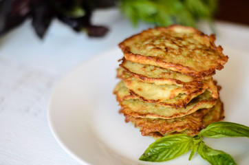 vegetarian zucchini pancakes, served with fresh herbs in the white plate and on the white wooden background