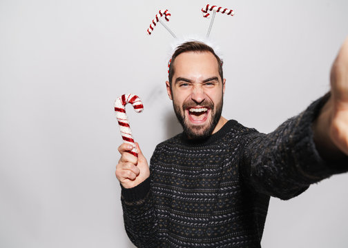 Image of man in New Year headband taking selfie with Christmas candy cane