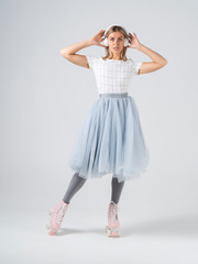 A young woman in retro quad roller skates listening to music and holds headphones a white cyclorama background