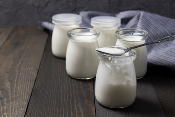Natural homemade yogurt in glass jars with spoon on dark wooden background