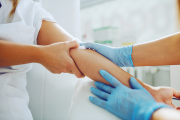 Close up of lab assistant putting absorbent cotton on patient arm after taking blood sample.