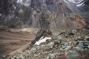 Atmospheric alpine landscape with firn or snow near stony cliff on snowy mountain wall background on combe rocky hill. Craggy mountainside of boulder stream close-up. Majestic scenery on high altitude