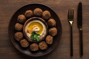 top view of falafel balls with hummus on plate near cutlery on wooden table