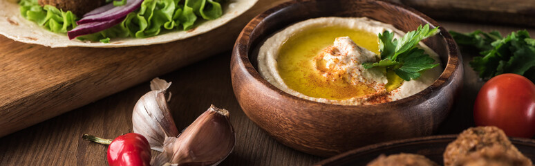 close up view of fresh hummus, spices and vegetables on wooden table, panoramic shot