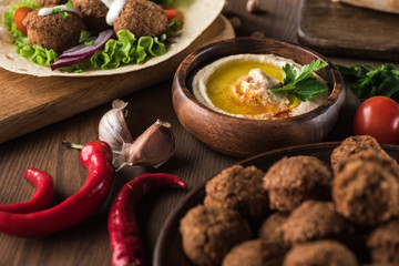 close up view of falafel near fresh hummus, spices and vegetables on wooden table