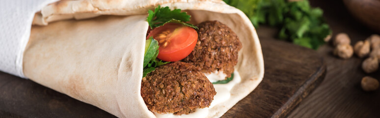 close up view of falafel with vegetables and sauce wrapped in pita on wooden table, panoramic shot