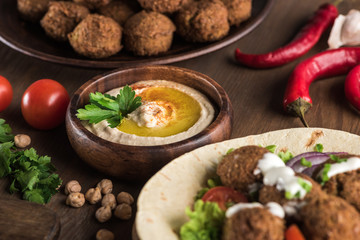 close up view of falafel with vegetables and sauce on pita near fresh hummus on wooden table