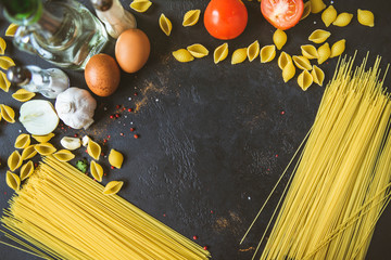 raw spaghetti and pasta in the form of shells, tomatoes, spices, eggs, garlic, oil on a black...