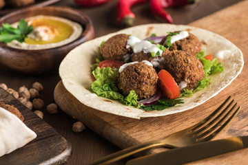 close up view of falafel on pita with vegetables and sauce near hummus on wooden table
