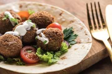 close up view of falafel with vegetables and sauce on pita on wooden table near cutlery