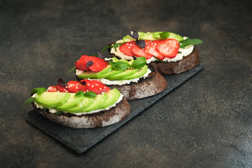 Toast or sandwich with avocado, cheese, strawberries, herbs and seeds on a dark background. An idea for bruschetta or for a healthy snack. Healthy vegan breakfast.