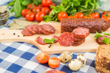 Sliced salami with cherry tomatoes and quail eggs on table