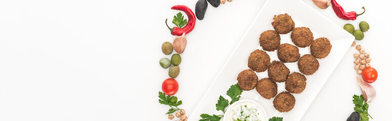 top view of vegetables arranged in round frame around falafel on plate with sauce on white background, panoramic shot
