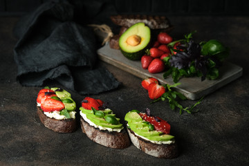 Toast or sandwich with avocado, cheese, strawberries, herbs and seeds on a dark background. An idea for bruschetta or for a healthy snack. Healthy vegan breakfast.