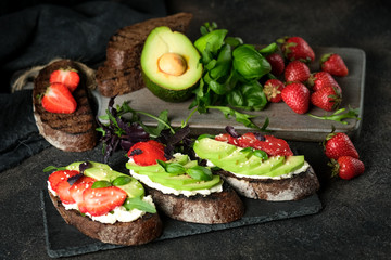 Toast or sandwich with avocado, cheese, strawberries, herbs and seeds on a dark background. An idea for bruschetta or for a healthy snack. Healthy vegan breakfast.