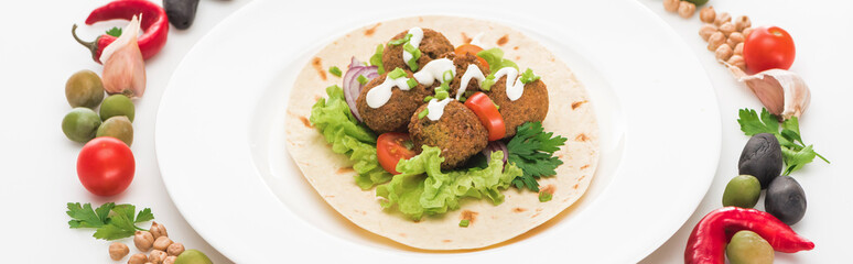 vegetables arranged in round frame around falafel on pita on plate on white background, panoramic shot