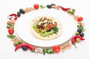 vegetables arranged in round frame around falafel on pita on plate on white background