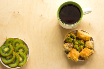 Cakes, kiwi slices in a plate and tea in a mug. On the wooden countertop are a mug of tea, a plate of sliced kiwi slices and a plate of Oriental sweets