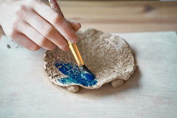 Unrecognised Woman making pattern on ceramic plate, hands close-up, focus on palms with paint brush. Creative hobby concept. Earn extra money, side hustle, turning hobbies into cash, passion into job