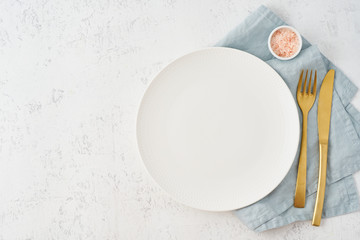 Clean empty white plate, fork and knife on white stone table, copy space, mock up, top view. Concept for menu