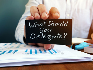 Businessman holds sign What Should You Delegate. Delegation concept.
