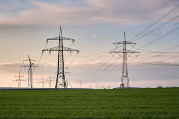 Stromtrasse, Hochspannungsmasten hintereinander aufgereiht bis zum Horizont auf einer grünen Wiese