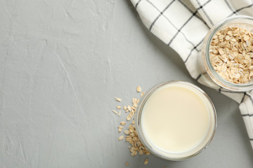Glass of oat milk, oatmeal seeds, napkin on grey background, space for text. Top view