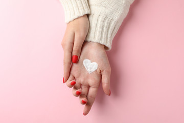 Woman hands, heart shape created from winter cream on pink background. Top view