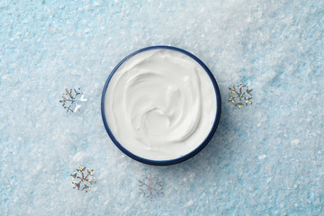 Jar of winter cream for skin on snowy blue background, space for text. Top view