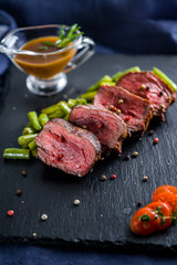 Steak medallion with vegetables and sauce on a black plate with coals