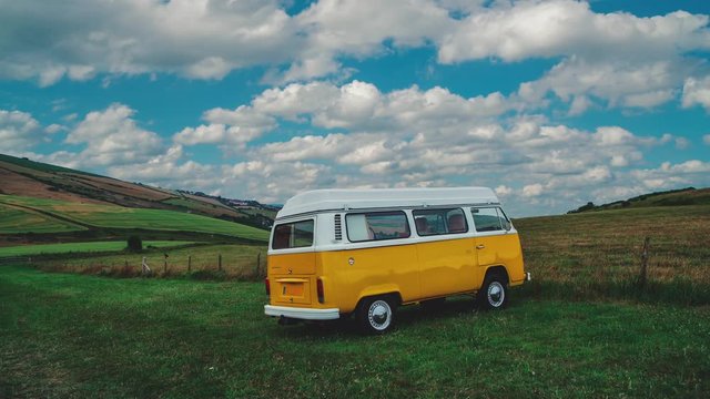 4K UHD Cinemagraph / seamless video loop of a classic T2 Bulli Camper Van standing on a green field on a sunny afternoon in England with blue sky, the clouds are moving by quickly.