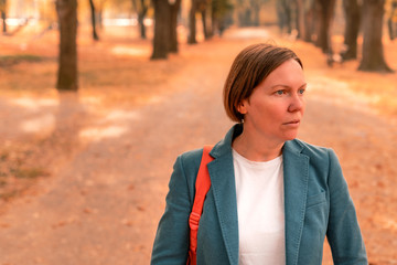 Portrait of businesswoman in autumn park, standing on footpath