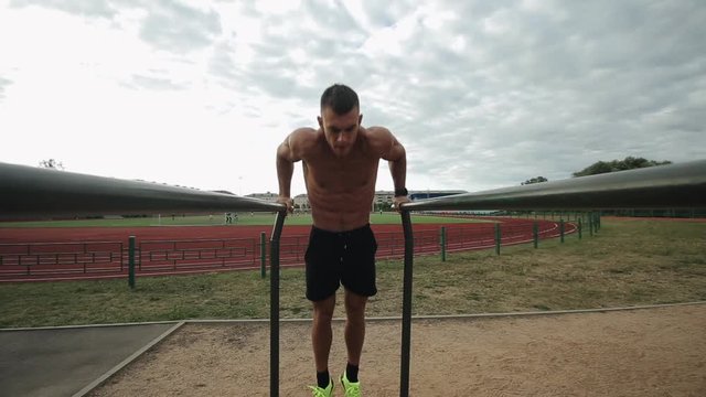 Good-looking sportsman doing push-ups on parallel bars on the outdoor stadium