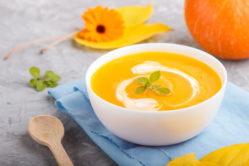 Traditional pumpkin cream soup with in white bowl on a gray concrete background with blue napkin. side view, selective focus.