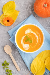 Traditional pumpkin cream soup with in white bowl on a gray concrete background with blue napkin. top view