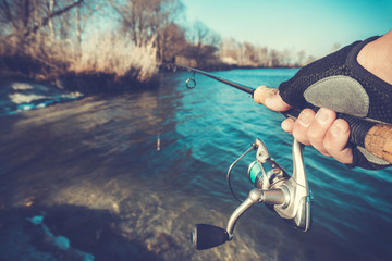 hand with spinning and reel on the summer lake
