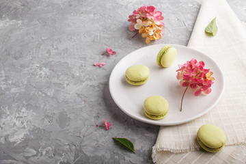 Green macarons or macaroons cakes on white ceramic plate on a gray concrete background  side view.