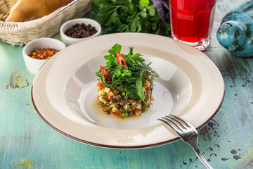 Baked eggplant, zucchini and pepper with parsley on top and glass of red drink on blue wooden table