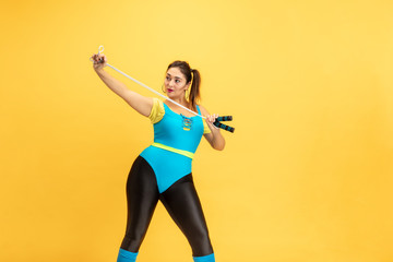 Fototapeta na wymiar Young caucasian plus size female model's training on yellow background. Stylish woman in bright clothes. Copyspace. Concept of sport, healthy lifestyle, body positive, fashion. Posing with jump rope.