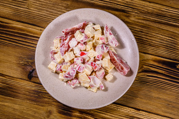 Salad with crab sticks, cheese and tomatoes dressed with mayonnaise on a wooden table. Top view