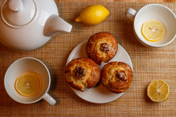 white teapot and two white cups of tea with lemon and muffins top view