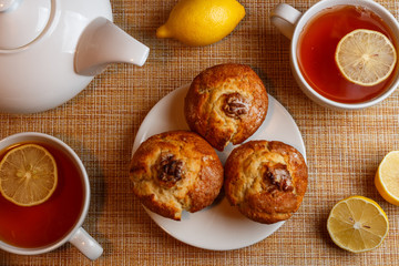 white teapot and two white cups of tea with lemon and muffins top view