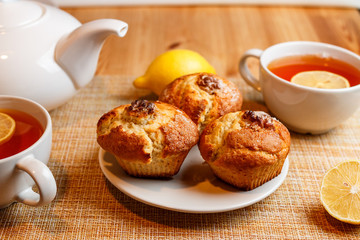teapot is white and two white cups of tea with lemon and muffins