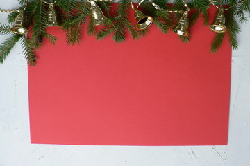 Fototapeta na wymiar Christmas decorative border with copy space for your text. Christmas golden toy bells and branches of a Christmas tree on a red background.