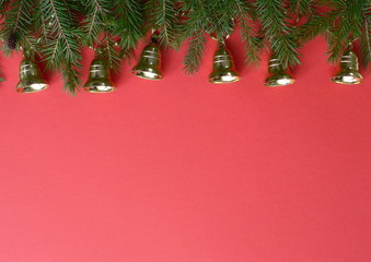 Christmas decorative border with copy space for your text. Christmas golden toy bells and branches of a Christmas tree on a red background.