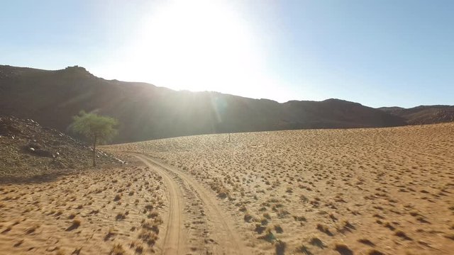 An empty desert track in Namibia with a blue sky and the sun.