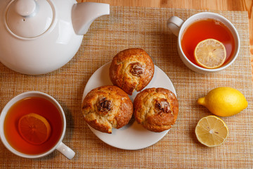 white teapot and two white cups of tea with lemon and muffins top view