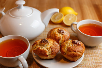 teapot is white and two white cups of tea with lemon and muffins